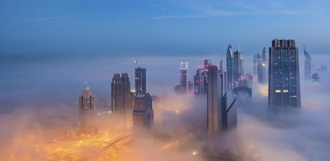 Stadtbild mit beleuchteten Wolkenkratzern über den Wolken in Dubai, Vereinigte Arabische Emirate, in der Abenddämmerung., lizenzfreies Stockfoto