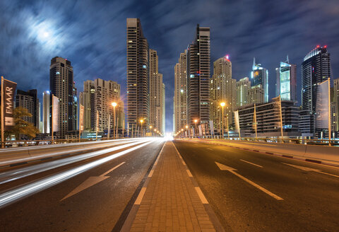 Stadtbild mit beleuchteten Wolkenkratzern in Dubai, Vereinigte Arabische Emirate, in der Abenddämmerung, im Vordergrund die Autobahn. - MINF07547
