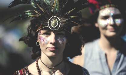 Junge Frau auf einem Sommer-Musikfestival, mit geschminktem Gesicht und Federkopfschmuck, schaut in die Kamera. - MINF07622