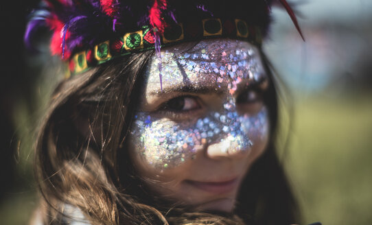 Young woman at a summer music festival face painted, wearing feather headdress, looking at camera. - MINF07623