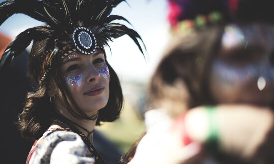Junge Frau auf einem Sommer-Musikfestival, mit geschminktem Gesicht und Federkopfschmuck, schaut in die Kamera. - MINF07624