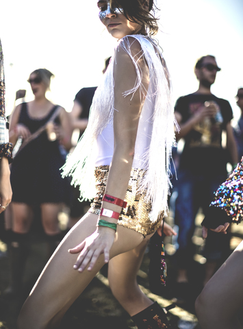 Junge Frau auf einem Sommermusikfestival, die goldene, mit Pailletten besetzte Hotpants trägt und in der Menge tanzt., lizenzfreies Stockfoto