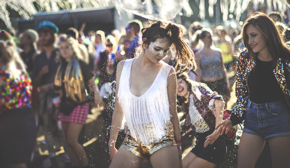 Junge Frau auf einem Sommermusikfestival, die goldene, mit Pailletten besetzte Hotpants trägt und in der Menge tanzt. - MINF07631