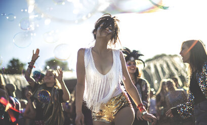 Young woman at a summer music festival wearing golden sequinned hot pants, dancing among the crowd. - MINF07634