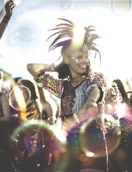 Young woman at a summer music festival wearing feather headdress, dancing among the crowd. - MINF07635