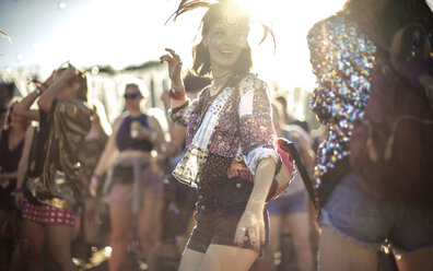 Young woman at a summer music festival wearing feather headdress, dancing among the crowd. - MINF07636