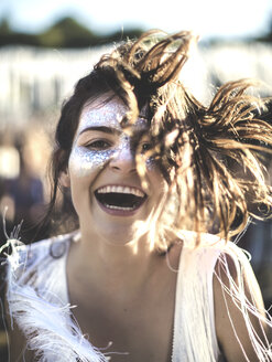 Young woman with long brown hair at a summer music festival face painted, smiling at camera. - MINF07638