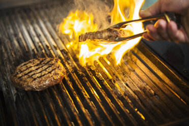 Close up of chef flame grilling a burger on a hot griddle. - MINF07658