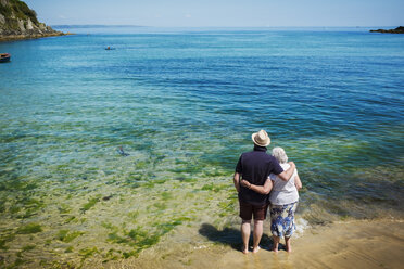 Rückansicht eines älteren Paares, das die Arme umeinander gelegt hat und auf das lebhafte blaue und türkisfarbene Wasser, den Ozean, blickt. - MINF07672