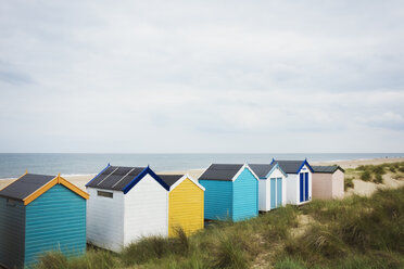 Eine Reihe bunt bemalter Strandhütten an einem Sandstrand unter einem bewölkten Himmel. - MINF07690