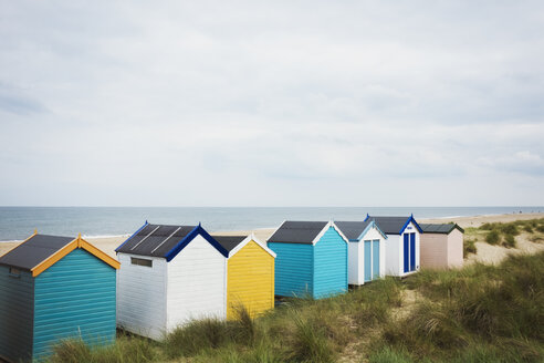 Eine Reihe bunt bemalter Strandhütten an einem Sandstrand unter einem bewölkten Himmel. - MINF07690