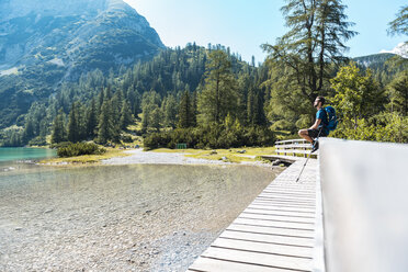Austria, Tyrol, Hiker at Lake Seebensee sitting on boardwalk, taking a break - DIGF04741