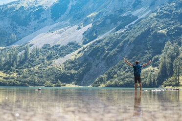 Österreich, Tirol, Wanderer am Seebensee knöcheltief im Wasser stehend, mit erhobenen Armen - DIGF04743