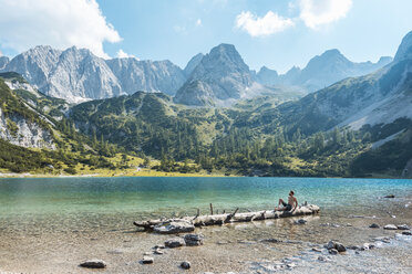 Österreich, Tirol, Junger Mann am Seebensee auf Baumstamm sitzend - DIGF04747