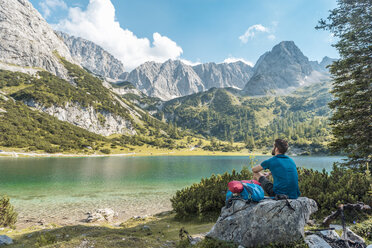 Österreich, Tirol, Wanderer macht eine Pause, sitzt auf einem Felsen und schaut auf einen See - DIGF04751