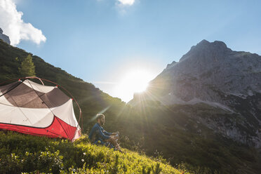 Österreich, Tirol, Wanderer macht eine Pause, sitzt im Gras neben seinem Zelt - DIGF04779