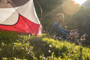 Österreich, Tirol, Wanderer macht eine Pause, sitzt im Gras neben seinem Zelt - DIGF04780