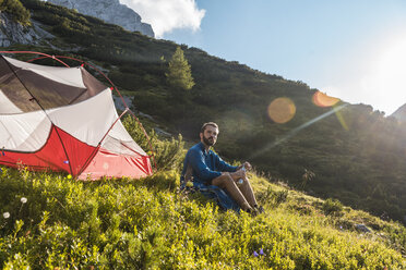 Österreich, Tirol, Wanderer macht eine Pause, sitzt im Gras neben seinem Zelt - DIGF04781