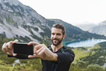 Österreich, Tirol, Wanderer macht Selfies mit seinem Smartphone am Seebensee - DIGF04790