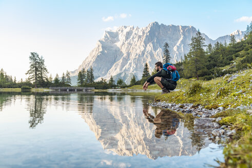 Austria, Tyrol, Hiker taking a break, crouching by the lake - DIGF04795