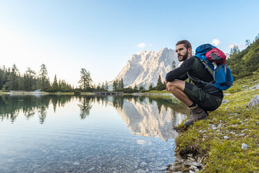 Austria, Tyrol, Hiker taking a break, crouching by the lake - DIGF04796