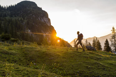 Österreich, Tirol, Wanderer mit Rucksack auf einer Wiese bei Sonnenuntergang - DIGF04799