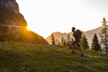 Austria, Tyrol, Hiker with backpack hiking in meadow at sunset - DIGF04800