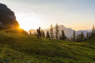 Austria, Tyrol, Hiker with backpack hiking in meadow at sunset - DIGF04801