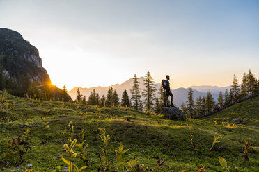 Österreich, Tirol, Wanderer mit Rucksack auf Felsen stehend, Sonnenuntergang betrachtend - DIGF04802