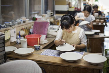 Women sitting in a workshop, working on Japanese porcelain bowls. - MINF07710