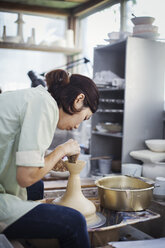 Frau bei der Arbeit in einer japanischen Porzellanwerkstatt, an der Töpferscheibe sitzend, beim Drehen einer Schale. - MINF07711