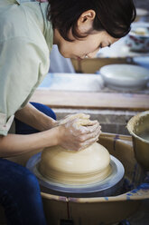 Woman working in a Japanese porcelain workshop, sitting at a potter's wheel, throwing bowl. - MINF07712