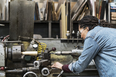 Frau mit Schutzbrille steht in einer Metallwerkstatt und arbeitet an einer Maschine. - MINF07764