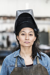 Portrait of woman wearing apron and welding mask standing in metal workshop, looking at camera. - MINF07767