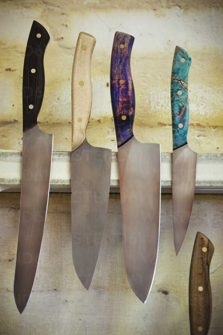 A Selection Of Knives With Shaped And Painted Wooden Handles On A Magnetic Knife Holder On A Workshop Wall MINF07791 