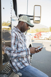 Ein schwarzer Lkw-Fahrer schreibt eine SMS, während er neben seinem auf einem Parkplatz geparkten Lkw steht. - MINF07808