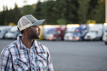 Black man truck driver near his truck parked in a parking lot at a truck stop - MINF07812