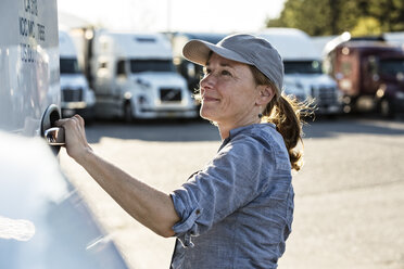 Caucasian female truck driver getting into her truck parked in a lot at a truck stop. - MINF07814