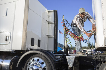 Black man truck driver attaching power cables from truck tractor to trailer at a truck stop. - MINF07815