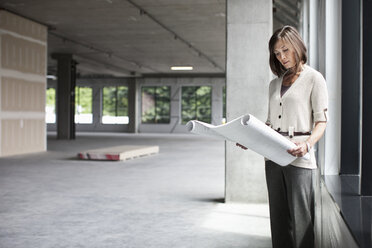 Caucasian businesswoman going over plans for a new office in a large empty raw office space. - MINF07820