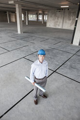 Caucasian businessman holding plans for a new office in a large empty raw office space. - MINF07822