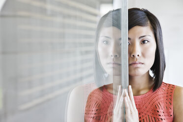 Eine asiatische Geschäftsfrau spiegelt sich auf einer Glaswand in einer Bürolobby. - MINF07833
