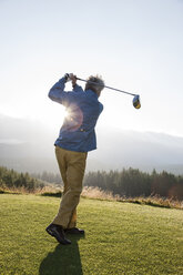 Ein asiatischer älterer Mann, der mit einem Golfschläger abschlägt. - MINF07834