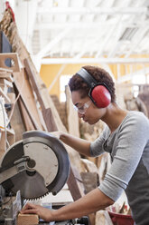 Schwarze Fabrikarbeiterin beim Schneiden von Holz mit einer Radialsäge in einer Holzverarbeitungsfabrik. - MINF07861