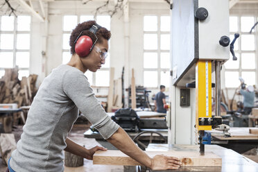 Schwarze Fabrikarbeiterin beim Schneiden von Holz mit einer Bandsäge in einer Holzverarbeitungsfabrik. - MINF07862