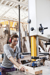 Black woman factory worker using a band saw to cut wood in a woodworking factory. - MINF07863