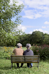 Ehemann und Ehefrau, Rückansicht eines älteren Mannes mit Hut und einer Frau, die nebeneinander auf einer Bank in einem Garten sitzen. - MINF07872