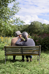 Ehemann und Ehefrau, Rückansicht eines älteren Mannes mit Hut und einer Frau, die nebeneinander auf einer Bank in einem Garten sitzen. - MINF07873