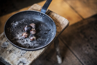 Nahaufnahme einer Bratpfanne mit frisch gerösteten Kastanien auf einem rustikalen Holztisch. - MINF07890