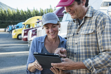 Caucasian woman and man truck driving team working on their driving log in a truck stop parking lot. - MINF07900